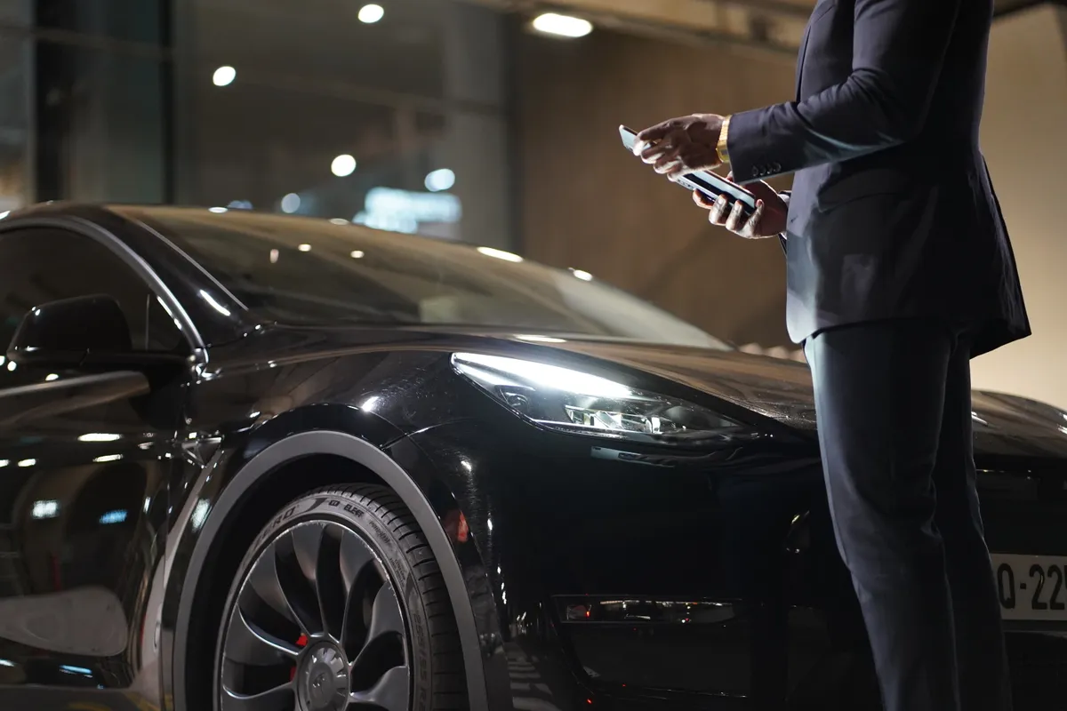 Your Obrigado Transports driver welcoming you beside a Tesla
